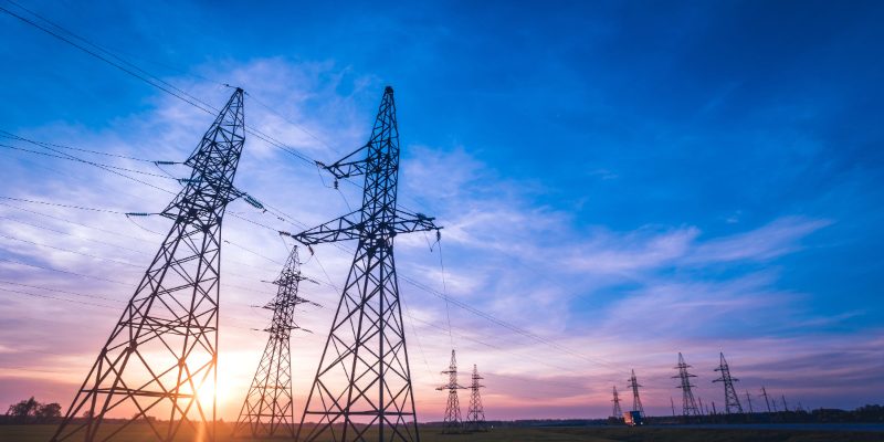 UK electricity transmission tower line at dusk — the grid asset class unlocked by Ofgem's RIIO-3 Final Determinations, with £28.1 billion of upfront funding inside a £90 billion pipeline.